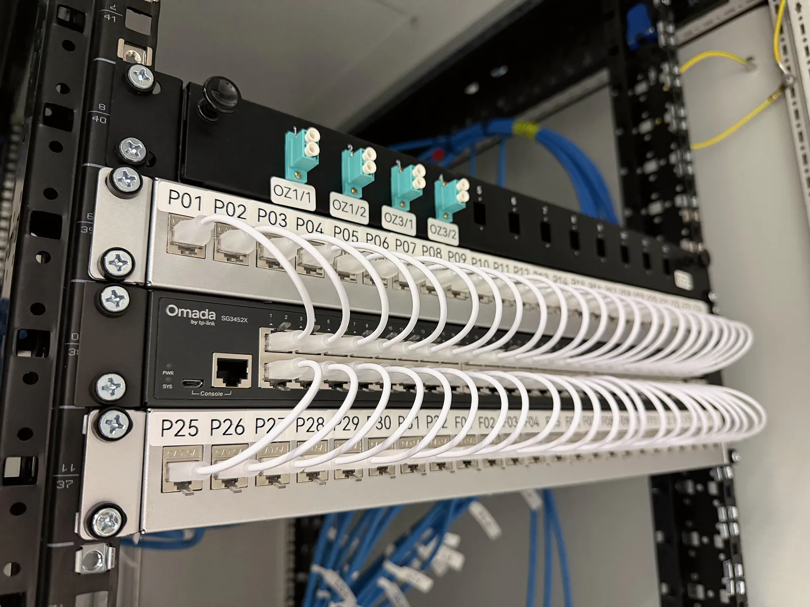 Feliratozott patch panel, Omada switch és optikai csatlakozók rendezett kábelezéssel