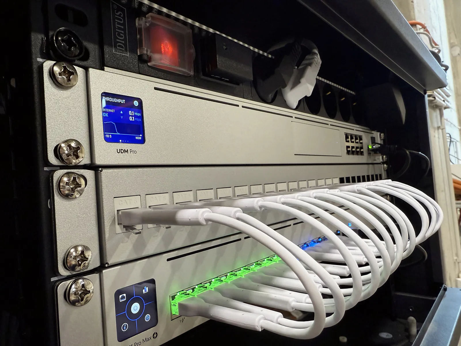 UniFi UDM Pro és switch rackszekrényben, rendezett fehér patchkábelekkel